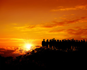 Wall Mural - group of silhoutted people on hill watching view over orange colored sunset sky