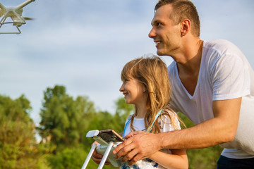 Young father shows his cute daughter how to control drone outdoors.