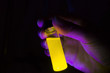 Woman researcher holding yellow photochemical reaction in glass vial under UV light in a dark chemistry laboratory