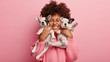 © wayhome.studio - Photo of joyful dark skinned lady with Afro haircut, feels fun, carries two little french bulldog puppies, expresses affection, have good relationship, owner feels responsibility. Pedigree pets