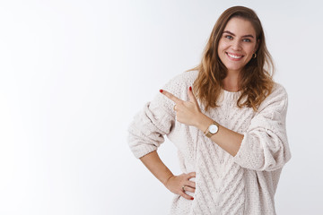Wall Mural - Friendly good-looking feminine young tall female model wearing cozy warm loose sweater pointing left sideways index finger suggesting try app product, smiling delighted indicating cool copy space