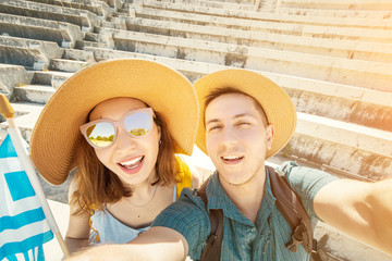 Wall Mural - European man and Asian girl in love a couple of tourists take a selfie in an ancient Greek Acropolis with a flag. Travel and adventure in Greece