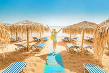 Girl Walking On The Beach With Sunbeds And Sun Umbrellas. Seaside Resort And Summer Vacation Concept