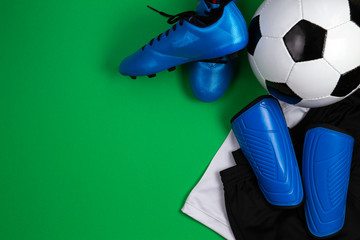 Soccer ball, blue boots, cleats, white t-shirt and black shorts on green background. Flat lay, top view