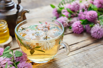 Wall Mural - Red clover flowers, healthy herbal tea cup, honey jar and vintage copper tea kettle on table.