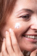 © HD92 - side view, close-up of one mature woman skin pores, applying skin cream to her face.