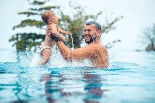 Dad Is Holding His  Baby Son In His Arms, While Having Fun In The Luxurious Pool. Family Vacation