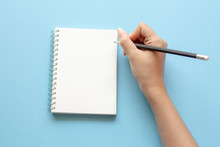 Woman Hands Writing In Empty Notebook At The Blue Desk. Flat Lay Top View. 