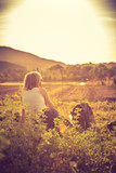 Fototapeta  - Enjoying the evening sun, sundown scenery: woman is sitting in the green grass