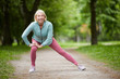 canvas print picture - Contemporary mature blonde female in activewear doing exercise for leg stretch while enjoying workout in natural environment