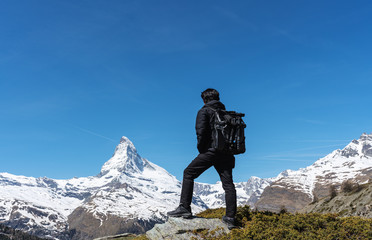 Wall Mural - travelling in switzerland, a man with backpack standing on the rock looking at matterhorn mountain v