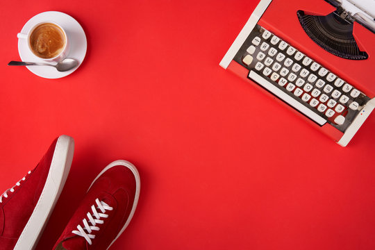Bright red shoes, typewriter and coffee cup on red background
