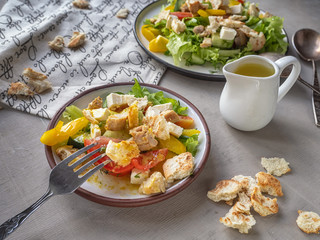 Caesar salad on two plates, large and small, jug with sauce and decorative linen napkin on a gray background. Near scattered croutons for salad.