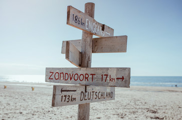 Wooden information board with distance to England, Germany and Zandvoort on the beach by the North Sea in Noordwijk, The Netherlands