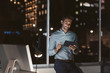 © mavoimages - Smiling businessman using a tablet in his office at night