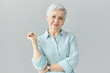 Isolated image of elegant fashionable middle aged European woman on retirement posing in studio wearing stylish striped blue shirt and wrist watch, having good day, smiling at camera happily