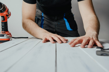 Poster - The man wraps wooden boards on the work table. The concept of DIY and renovation of new things. A man tinkering at home, working with wood.