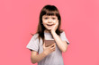 © Marharyta Hanhalo - Portrait of a shocked young little child girl looking at mobile phone isolated over pink background. Overjoyed happy excited kid.  rejoices good news, stares at mobile phone, gestures actively