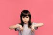 © Marharyta Hanhalo - Portrait of a beautiful young little girl child wearing grey t-shirt standing isolated over pink background, presenting copy space down here and having bad sad melancholy expression.