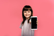 © Marharyta Hanhalo - Surprised happy dark haired little girl kid showing smartphone with blank screen and smiling isolated over pink studio background.