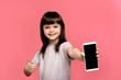 © Marharyta Hanhalo - Indoor portrait of attractive young little child girl isolated on pink background, holding blank smartphone, smiling at camera, showing screen, feeling happy and surprised. Human emotions