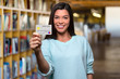 © elnariz - Smiling college university student holding mockup new bank credit card in library to assist her through education