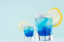 Bright Summer Fresh Blue Fruit Cocktail With Blue Curacao Liquor, Ice Cubes, Sugar Rim, Lemon Slice In Pastel Mint Color Interior On White Wood Board.