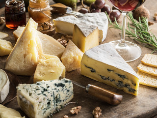 Wall Mural - Cheese platter with organic cheeses, fruits, nuts and wine on wooden background. Tasty cheese starter.