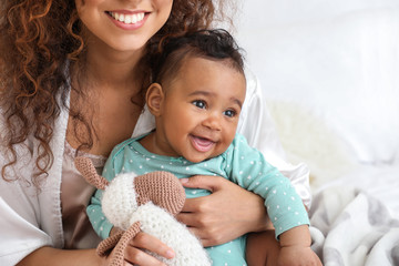 Happy African-American mother with cute little baby in bedroom