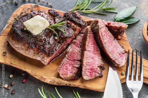 Fotografía Medium rare Ribeye steak with herbs and a piece of butter on the wooden tray