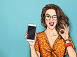 Winking woman in glasses showing smart pone and OK sign. Pop art girl holding phone. Digital advertisement female model showing the message or new app on cellphone.