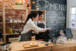 © PR Image Factory - first part time job in summer concept. professional barista teaching young girl new employee how to using tablet to take customer order in cafe bar counter in coffee shop. coworkers help each other