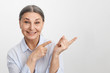 © shurkin_son - Isolated studio image of charismatic excited elderly female Human Resources expert with gray hair pointing index fingers to the right and smiling broadly, friendly showing you way to success