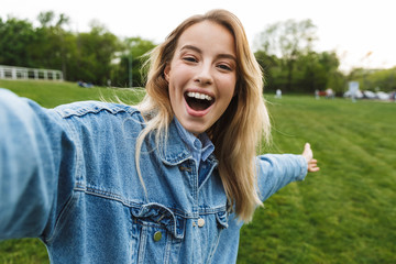 Poster - Photo of happy amazed woman taking selfie photo and smiling at camera while walking in green park