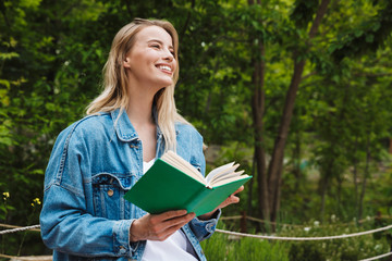 Canvas Print - Photo of nice happy woman reading book while sitting on bench in green park