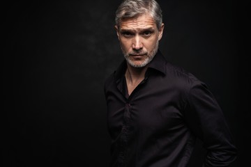 middle-aged good looking man posing in front of a black background with copy space.