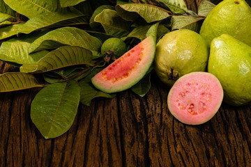 Fresh red guavas with green leaves on wooden demolition background. Wood texture and guava leaves.