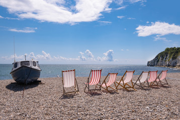 Deckchairs and boat on shingle beach at Beer, Devon, United Kingdom