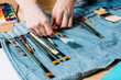 © golubovy - Painter kit. Closeup of artist hands choosing paintbrush. Handmade denim bag organizer.