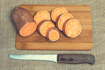 Wall Mural - Sliced raw sweet potatoes on a wooden cutting board. Product photo of batats. Healthy diet for vegetarians and vegans. Source of vitamins. Wooden plank with batatas and knife