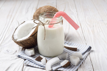 Wall Mural - Mason jar of milk or yogurt on blue napkin on white wooden table with coconut aside