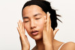 © leandro crespi/Stocksy - Young natural asian woman portrait applying moisturiser.