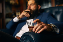 Man holding rum glass while sitting on chair