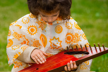 central park of the city. A young child is playing the gusli, psaltery -ancient traditional russian folk instrument. Horizontal view.