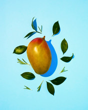 Flat Lay View Of A Single Yellow Mango With Green Leaves On A Blue Background.
