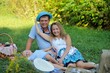 © alexbard - Happy family having fun playing sitting in the Park on a summer day. Mom puts on dad's women's hat and laughs with his son. Family picnic in nature. Portrait. Horizontal view