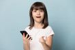 © fizkes - Little girl hold smartphone looking at camera feel surprised
