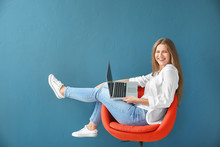 Beautiful Young Woman With Laptop Sitting On Chair Against Color Background