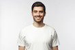 Portrait of smiling young man in white t-shirt looking at camera, isolated on gray background