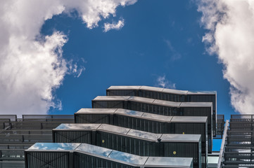 Business building with metal emergency ladder / fire escape in modern office buildings with repeating structure and reflected sky and clouds.